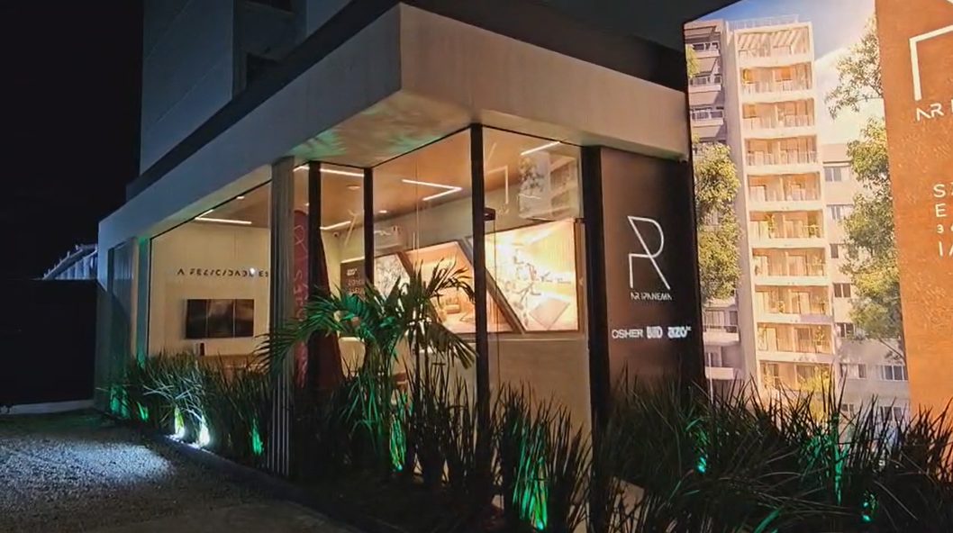 Fachada iluminada à noite do stand de vendas executado para a AZO inc., com vitrine de vidro e paisagismo